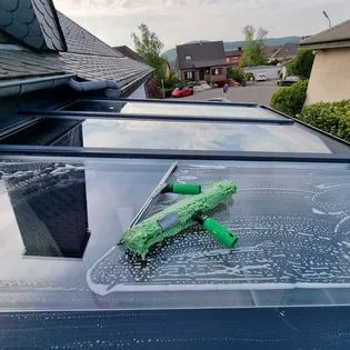 Une raclette et un chiffon de nettoyage sur une verrière savonneuse.