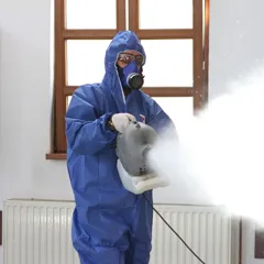 Une personne en tenue de protection utilise une machine de nettoyage à vapeur à l’intérieur.