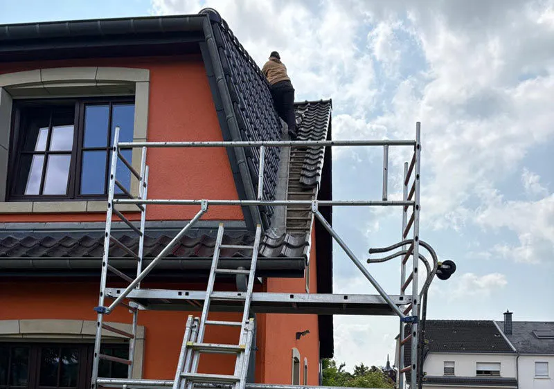 Couvreur travaillant sur une toiture en tuiles à côté d’un échafaudage.
