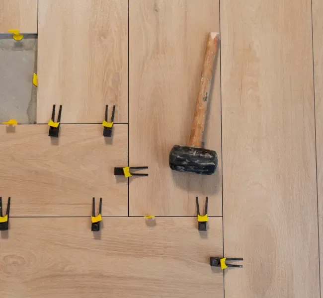 Holzbodenplatten werden mit Abstandhaltern und einem Gummihammer ausgerichtet.