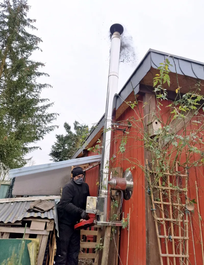 Worker servicing an exterior chimney beside a house.