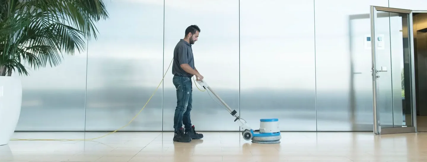 A person operates a floor-cleaning machine in a bright interior.
