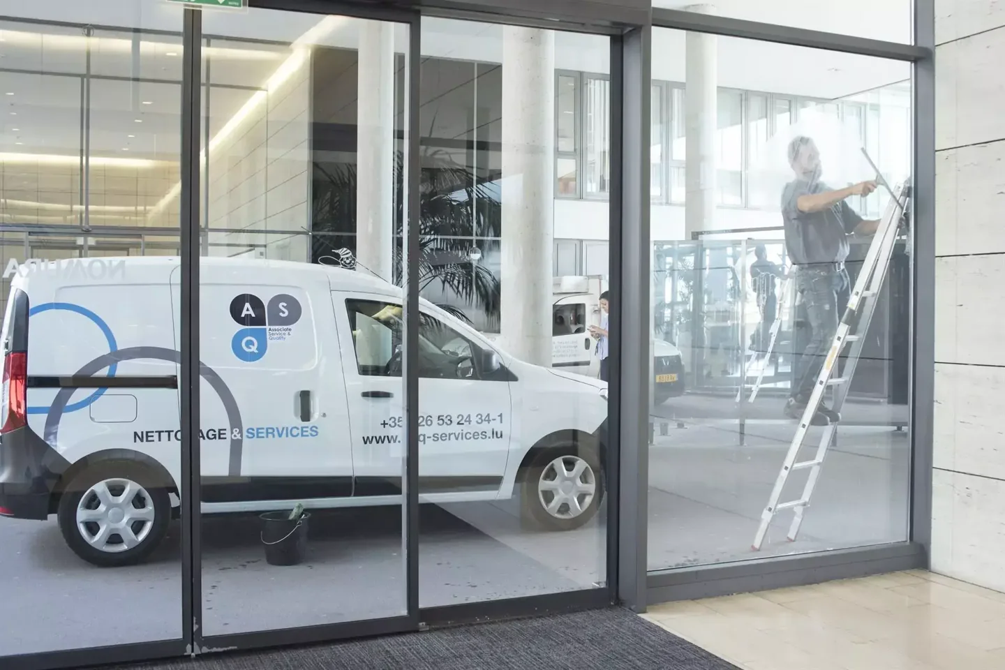 A person cleans glass doors beside a service vehicle.