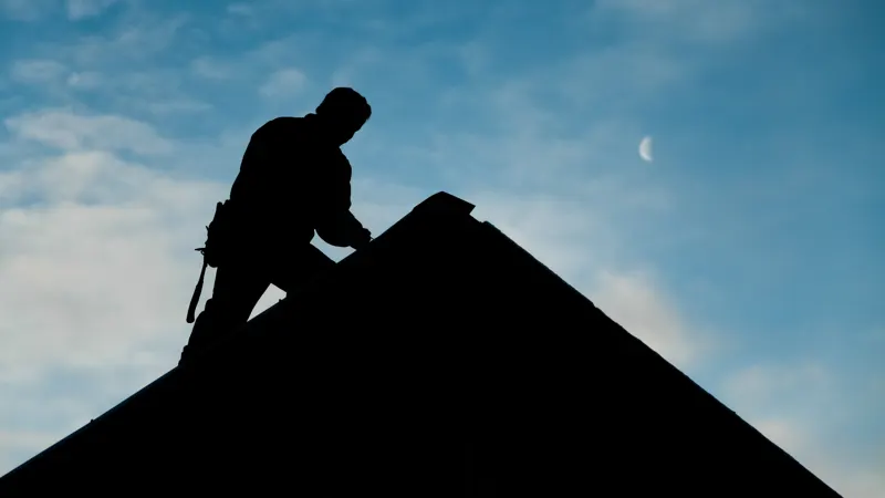Worker silhouetted on a roof against the sky.