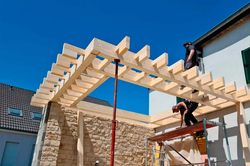 Workers building a timber roof structure with scaffolding.