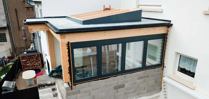 Flat-roof extension under construction beside a house.
