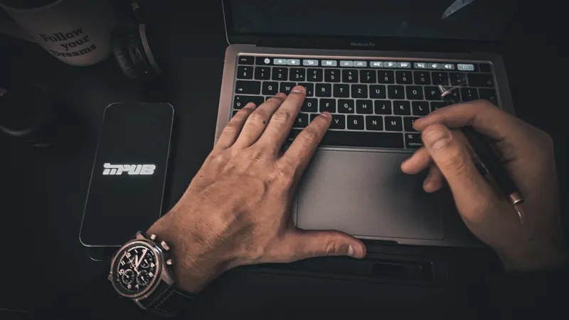 Hands typing on a laptop beside a smartphone.