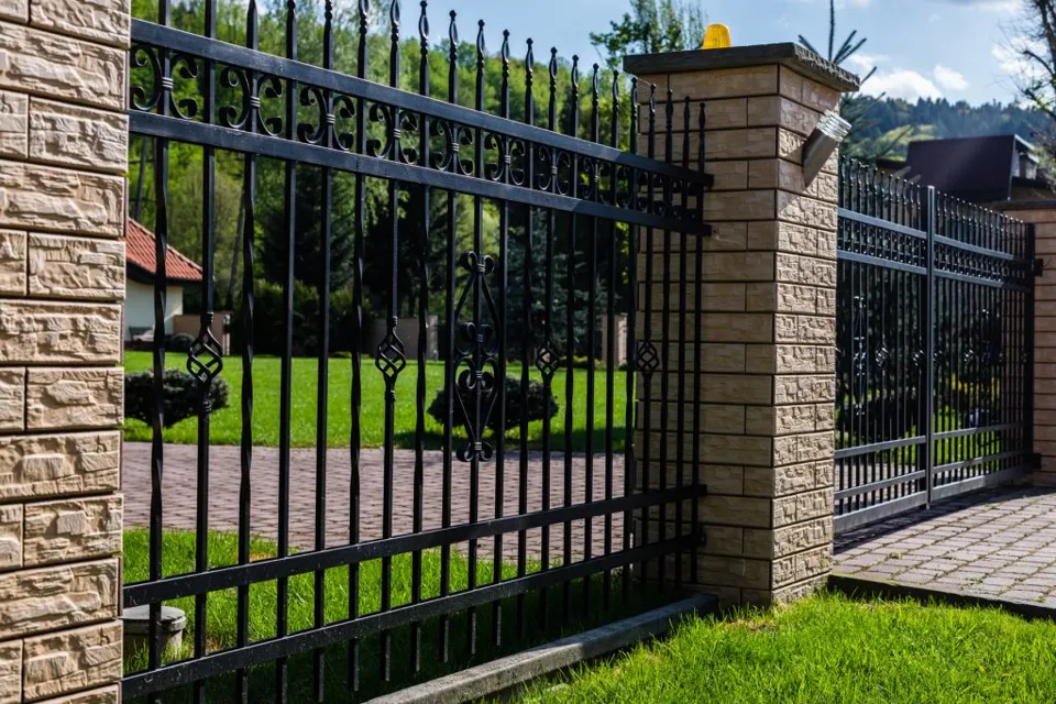 Black metal garden gate and fence with stone pillars.