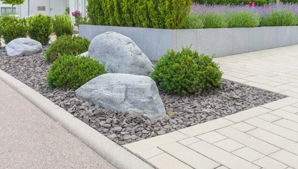 Paved garden area with stone planting beds and shrubs.