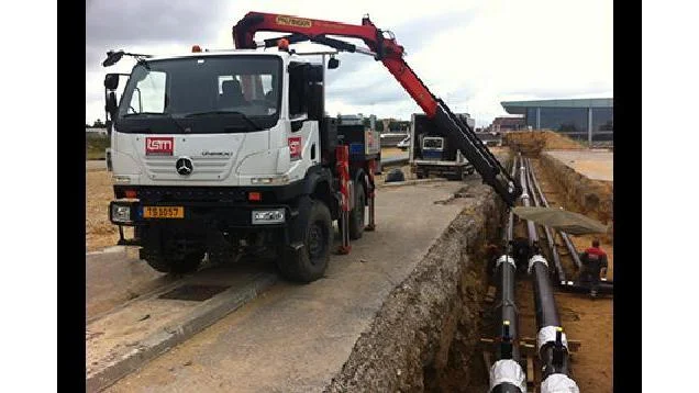 Crane truck laying pipes in a trench beside the road