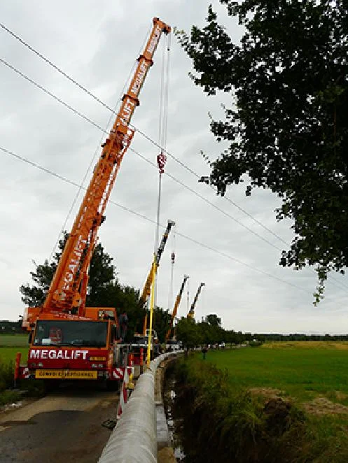 Crane lowering pipe sections along a rural road