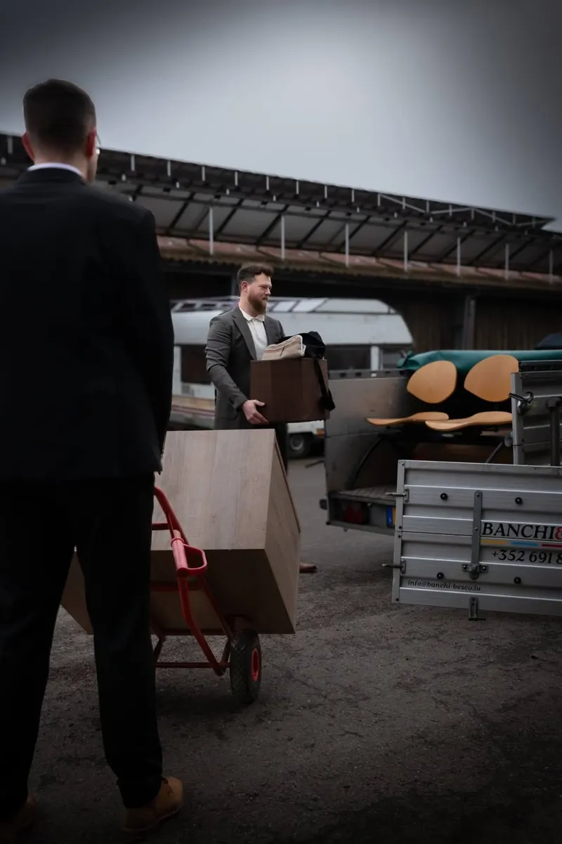 People moving furniture and panels with a hand truck near a trailer.