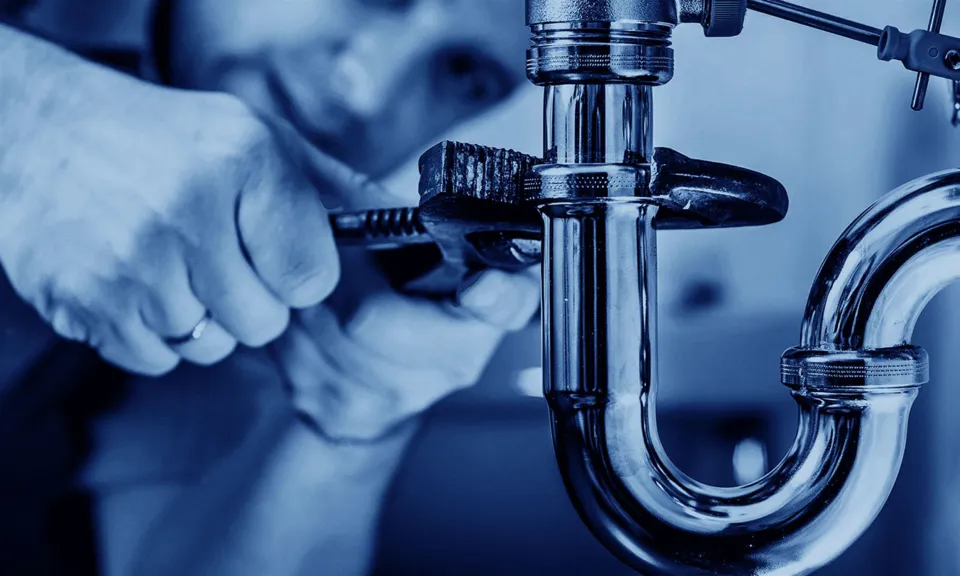 A technician repairs a pipe under a sink.