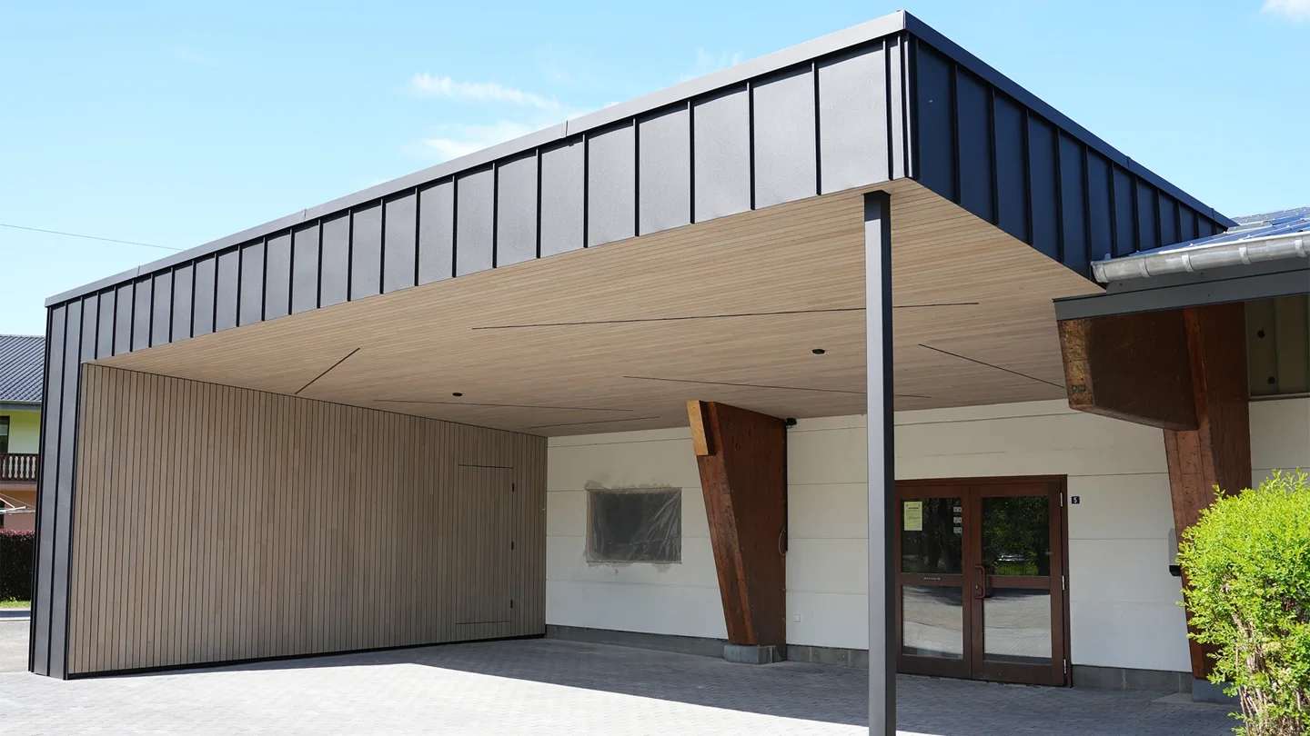 Timber entrance canopy with flat roof and dark standing-seam façade