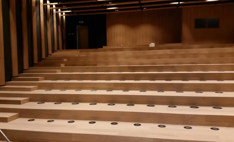 Tiered wooden auditorium seating with integrated floor fixtures.