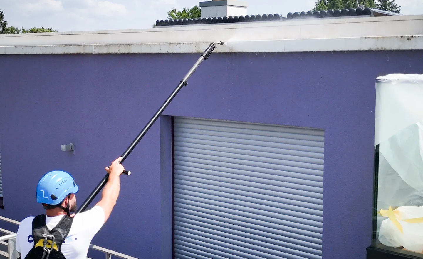 Cleanix technician cleaning a rendered façade with a telescopic lance