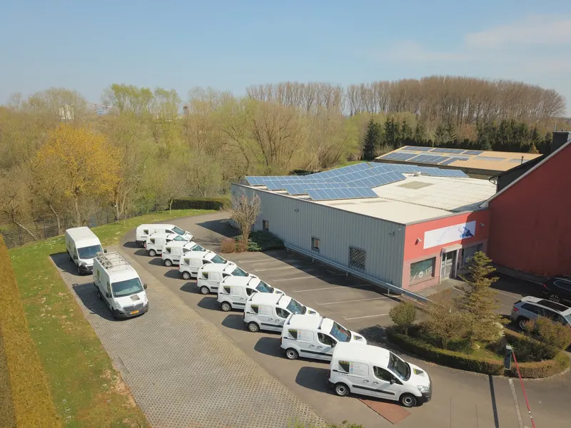 Aerial view of a commercial building with rooftop solar panels and parked vans.